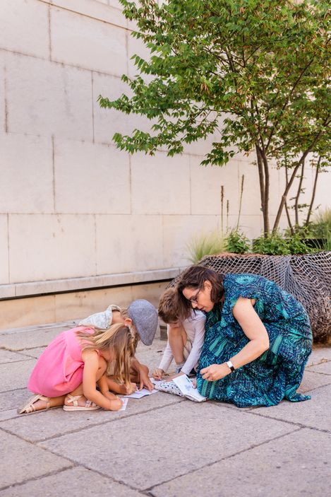 Eine Familie sitzt auf dem Boden im MuseumsQuartier und löst gemeinsam die Aufgaben des MQ-Rätselparcours.