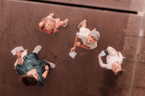 Draufsicht auf eine Familie im Innenhof des MuseumsQuartiers, die während des MQ-Rätselparcours nach oben blickt und ihre Rätselhefte in den Händen hält.
