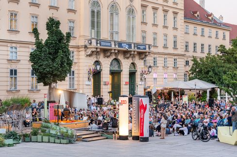 Large crowd seated in front of a historic building at an outdoor event with stage and lighting