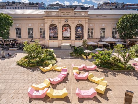 Halle E+G im MuseumsQuartier Wien mit üppig begrünten Flächen und gelben und rosa MQ Möbeln im Haupthof.