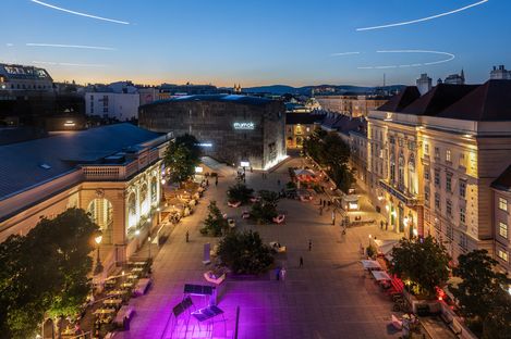 View across MuseumsQuartier Wien at dusk with mumok, Halle E+G, the green main courtyard, and MQ furniture.