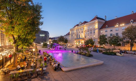 Haupthof des MuseumsQuartier Wien am Abend mit Wasserbecken, Gastronomie, Begrünung, mumok und Besucher:innen.