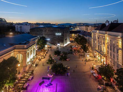 Blick über das MuseumsQuartier Wien in der Abenddämmerung mit mumok, Halle E+G, begrüntem Haupthof und MQ Möbeln.