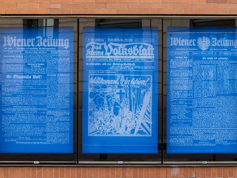 Hinter Vitrinenkästen befinden sich blaue Plakate mit weißer Schrift, die alte Zeitungsartikel zeigen.