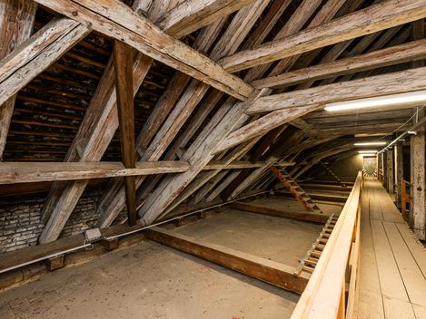 Langer Dachboden mit Holzbalkenkonstruktion, Laufsteg und Beleuchtung, der in die Tiefe des Raums führt.