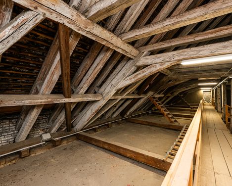 Long attic space with wooden beam construction, a walkway and lighting leading into the depth of the room.
