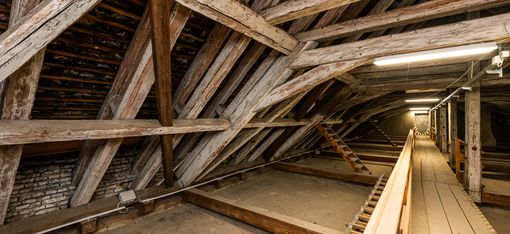 Long attic space with wooden beam construction, a walkway and lighting leading into the depth of the room.