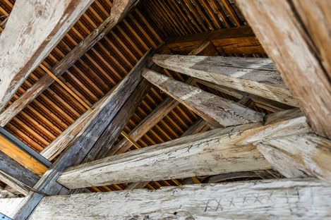 Upward view into the attic roof with intersecting wooden beams and tiled roofing.