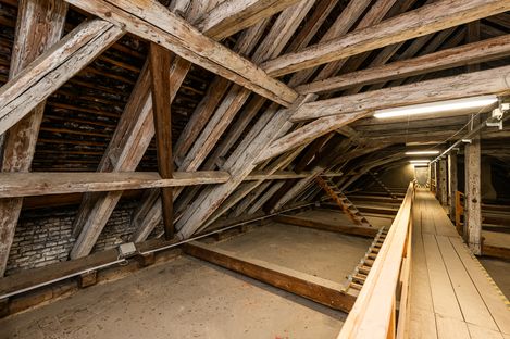 Long attic space with wooden beam construction, a walkway and lighting leading into the depth of the room.