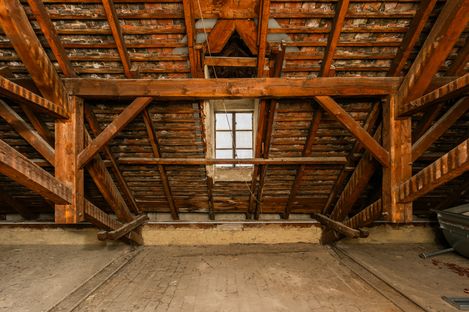 View into a historic attic roof structure with exposed wooden beams and bricks; a small window centred in the roof.