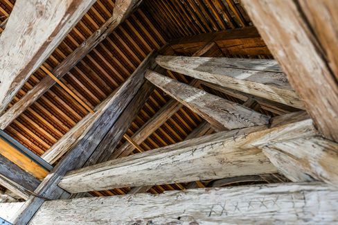 Upward view into the attic roof with intersecting wooden beams and tiled roofing.