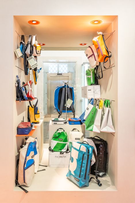 Präsentationsnische mit bunten Taschen und Rucksäcken verschiedener Größen, ausgestellt auf Regalen und Podesten.