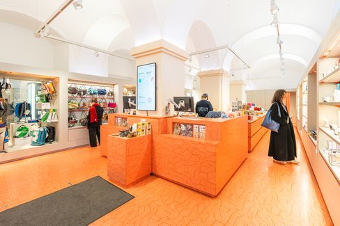 Museums­shop mit zentralem orangefarbenem Verkaufstresen, Gewölbedecke und Besucher:innen zwischen Regalen mit Designartikeln.