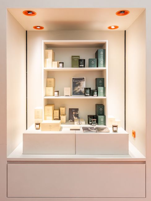 Produktdisplay mit Parfüms, Kerzen und Designartikeln auf weißen Regalen in einer beleuchteten Wandnische.