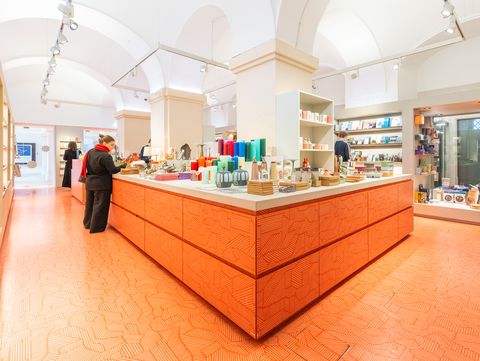 Museum shop with a central orange counter and visitors browsing design products and books.
