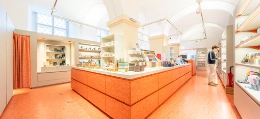 Large sales area of the MQ Point shop with a central counter and a visitor browsing products on the shelves.
