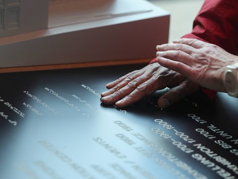 Two hands touching a black panel with white text, a window in the background.
