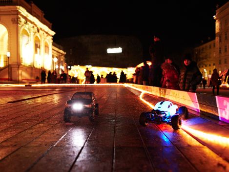 MQ Winter Race, MuseumsQuartier Wien. Zwei kleine elektrische Autos stehen in einer Rennbahn im MQ Hof. Menschen betrachten das Spektakel.