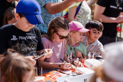 Children sit at a table, focused on crafting small boats and figures from paper and wood.