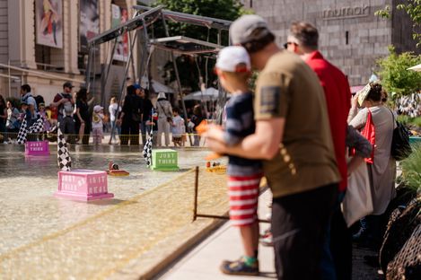 Visitors stand at the edge of a water basin watching a race of small model boats.