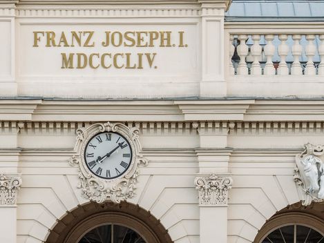 Fassade einer ehemalige Winterreithalle im MuseumsQuartier Wien mit der Inschrift 'FRANZ JOSEPH I. MDCCCLIV.' und einer Uhr über drei Rundbögen