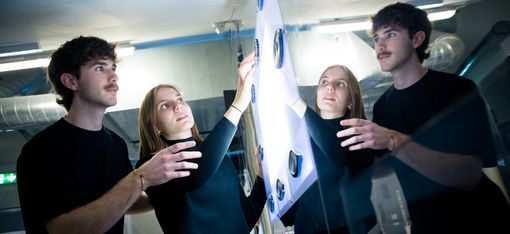 Two people interact with a glowing installation, their reflections visible in a glass surface.