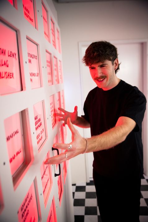 Two people interact with a glowing installation, their reflections visible in a glass surface.