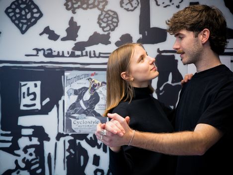 Two people dance closely together in front of a graphic-designed wall in an interior space.