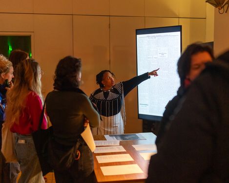 A woman points to a screen, surrounded by people watching her.