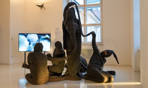 Textile sculptural installation with human-like figures in front of a video projection in a contemporary exhibition at MuseumsQuartier Vienna