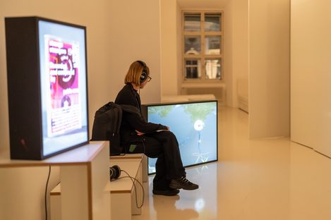 Visitor wearing headphones sitting in front of a video installation in a contemporary exhibition at MuseumsQuartier Vienna