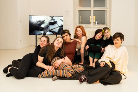 Group of six people sitting and lying on the floor in front of a screen in a bright room with a window and radiator.
