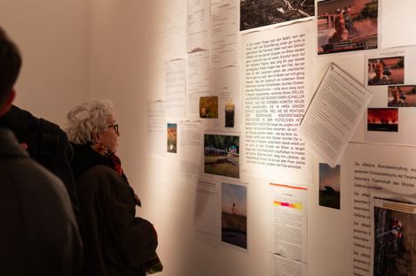 Exhibition visitors reading and viewing a text-based art installation with photographs and video stills at MuseumsQuartier Vienna