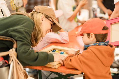A child and a woman are sitting at a table playing with a wooden frame and colorful stones.