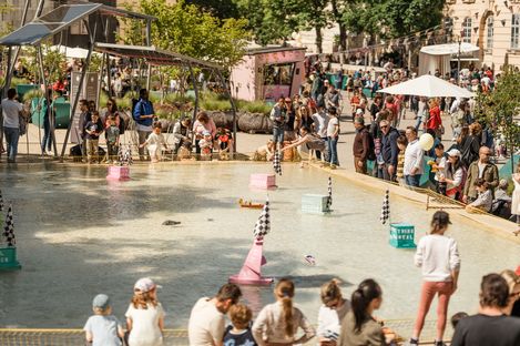 Families and children gather around a water basin where small handmade boats race against each other.