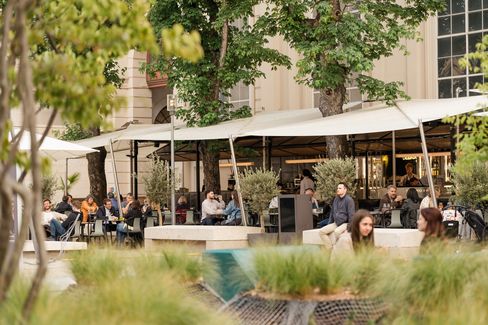 Visitors walk through the courtyard of MuseumsQuartier Vienna, with a lively outdoor dining area under sun shades in the background.