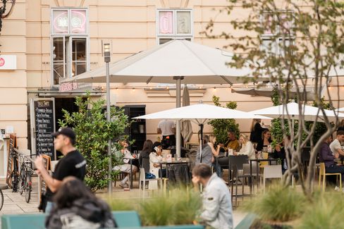 Large outdoor seating area at MuseumsQuartier Vienna with many visitors at tables and standing areas under sun umbrellas.