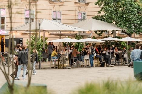 Outdoor café area at MuseumsQuartier with set tables, sun umbrellas and guests in front of a historic façade.