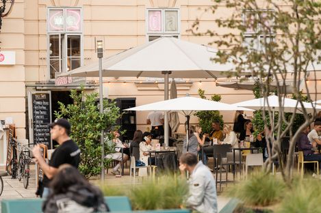 Large outdoor seating area at MuseumsQuartier Vienna with many visitors at tables and standing areas under sun umbrellas.