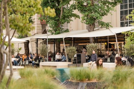 Visitors walk through the courtyard of MuseumsQuartier Vienna, with a lively outdoor dining area under sun shades in the background.