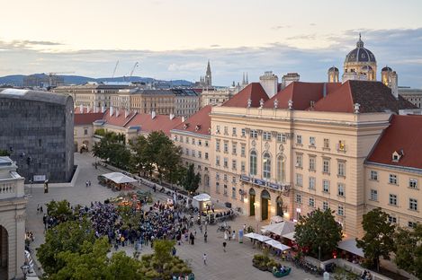 View of a busy square with people in front of historic buildings and a dome in the background at dusk