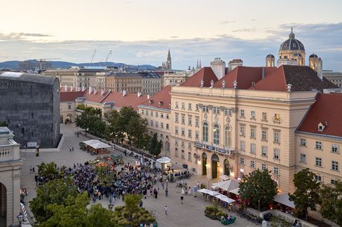 View of a busy square with people in front of historic buildings and a dome in the background at dusk
