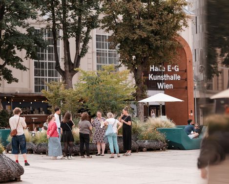 Gruppe von Menschen steht im Freien vor einem Gebäude mit der Aufschrift 'Halle E+G Kunsthalle Wien'