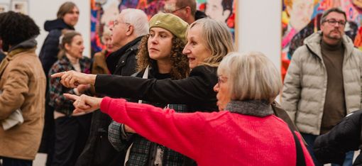 Drei Personen unterhalten sich und zeigen auf ein Bild in einer Ausstellung.