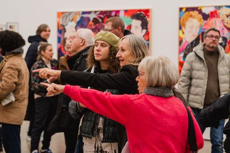 Three people are talking and pointing at a painting in an exhibition.