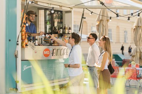 Three people stand at a food truck with the sign 'MQ Amore' and receive drinks from a server.