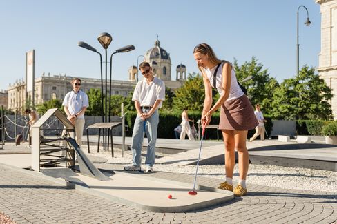 Several people play mini golf at a temporary course in MuseumsQuartier Vienna, surrounded by green areas.