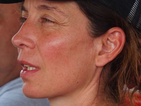Nahaufnahme einer Frau mit dunklem Netzcap, die nach links blickt, im Hintergrund unscharf ein Mann