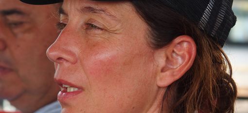Close-up of a woman wearing a dark mesh cap looking to the left with a blurred man in the background