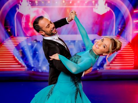 Ein Paar in eleganter Tanzpose auf einer Bühne mit buntem Hintergrund und Treppen